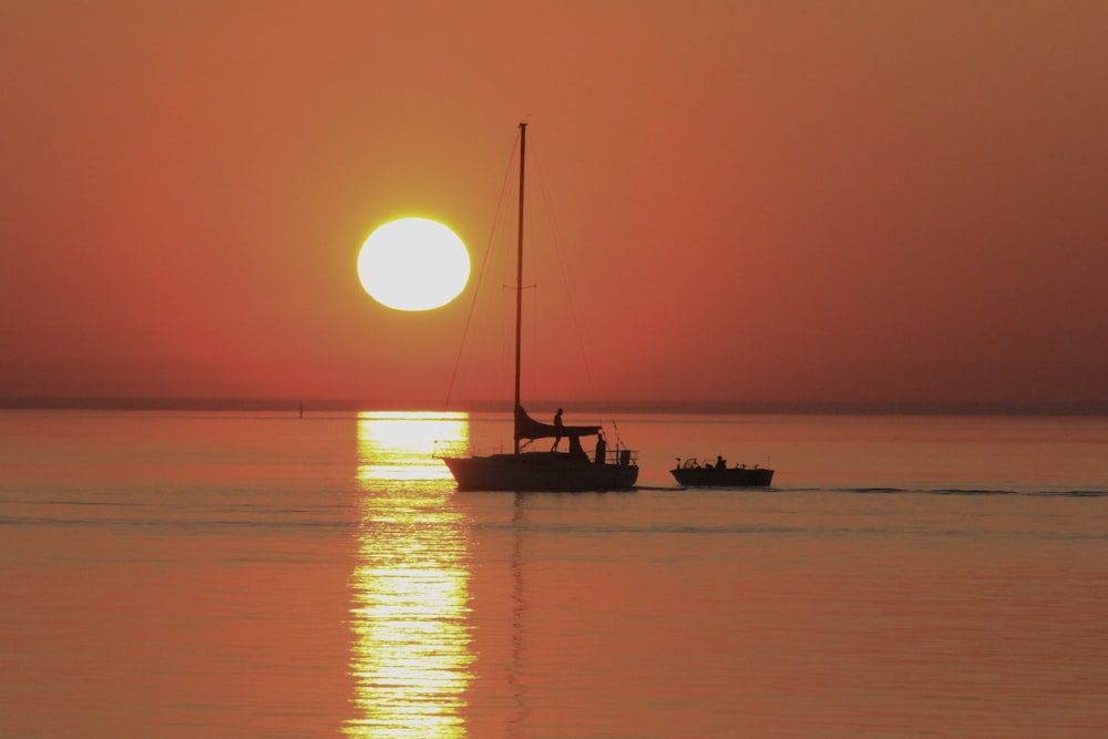 silhouette photography of boat floating in the sea during golden hour