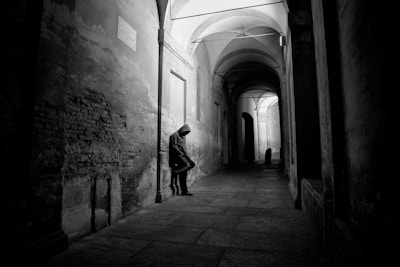 grayscale photo of man in hoodie leaning on alley wall