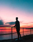 A silhouette of a woman standing by a balcony overlooking the Garonne river at sunset.