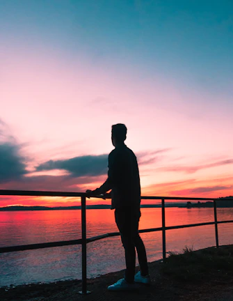 A silhouette of a woman standing by a balcony overlooking the Garonne river at sunset.