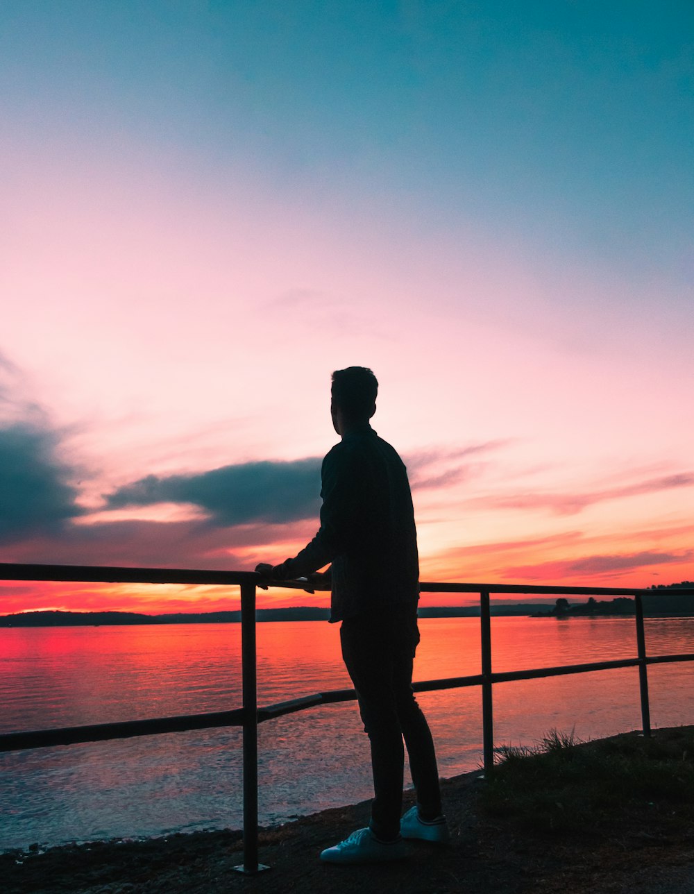 silhouette photography of man leaning against metal fence