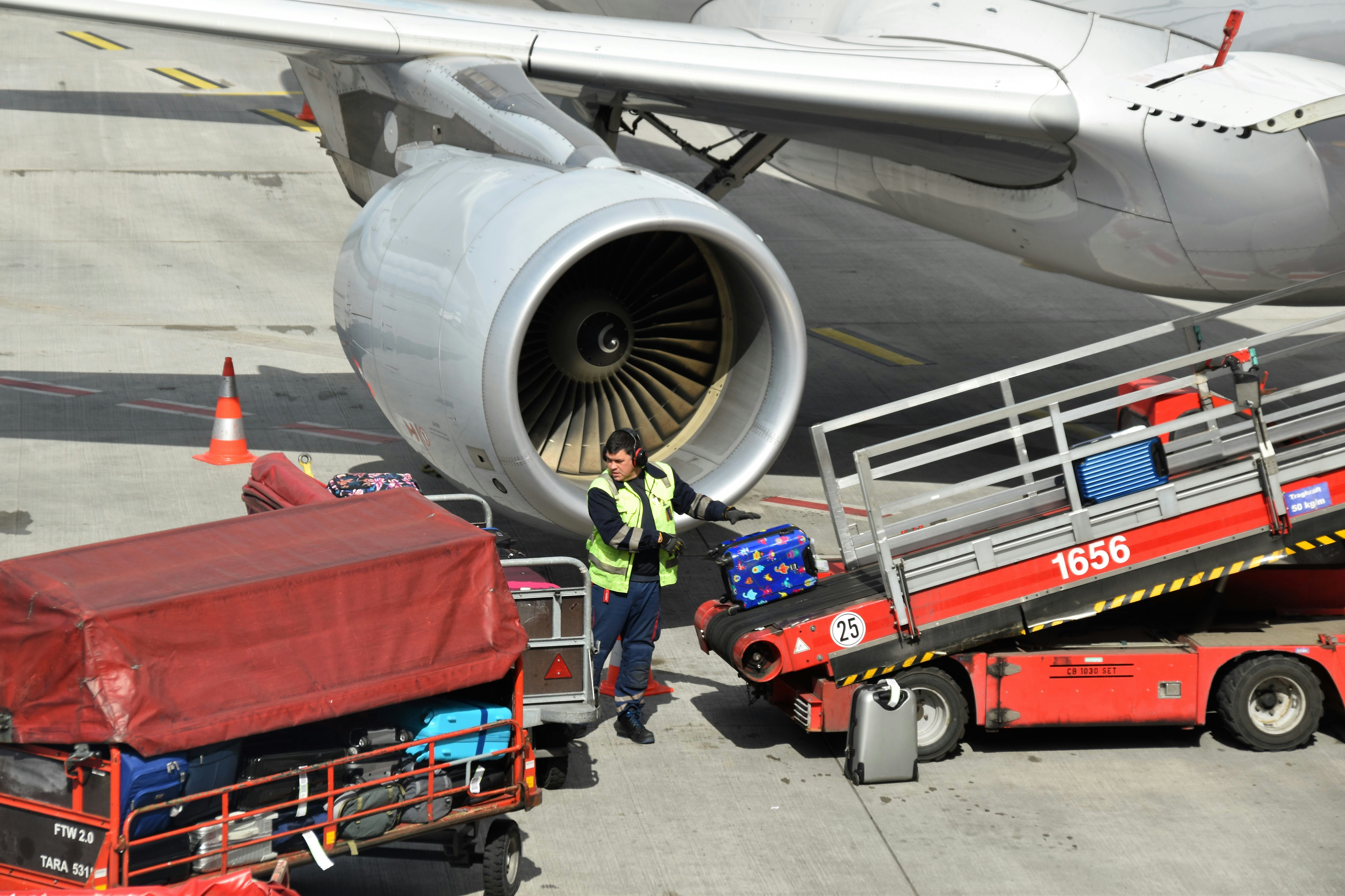 Airport ramp agent loading baggage onto aircraft conveyor belt, tarmac environment, daytime operations