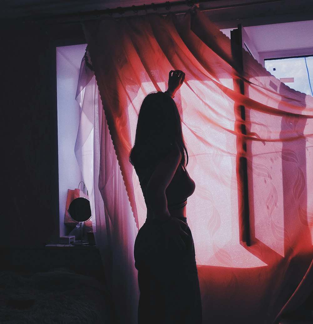 woman standing beside window with curtain