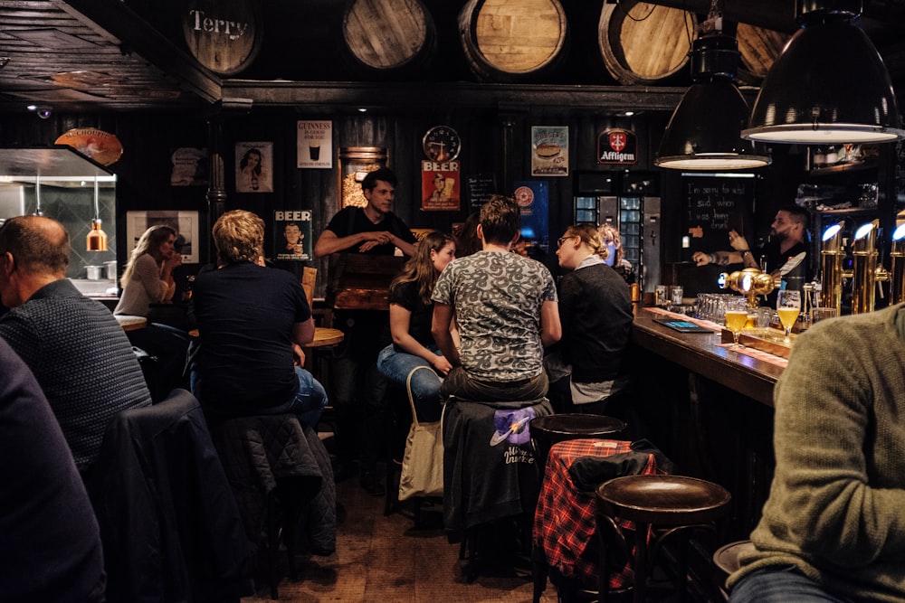 pessoas sentadas em cadeiras de bar enquanto bebem e conversam