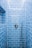A shower area with glossy blue subway tiles covering the walls. A modern chrome showerhead is attached to a metallic pipe on the right wall, and a sleek, round temperature control is centered on the wall. The tiles are neatly aligned, creating a clean and contemporary appearance.