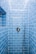 A shower area with glossy blue subway tiles covering the walls. A modern chrome showerhead is attached to a metallic pipe on the right wall, and a sleek, round temperature control is centered on the wall. The tiles are neatly aligned, creating a clean and contemporary appearance.