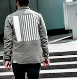 Model wearing the pine olive jacket standing against a minimalist urban backdrop.