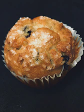 Close-up of a moist, fluffy high-protein muffin topped with blueberries and a light dusting of powdered sugar.
