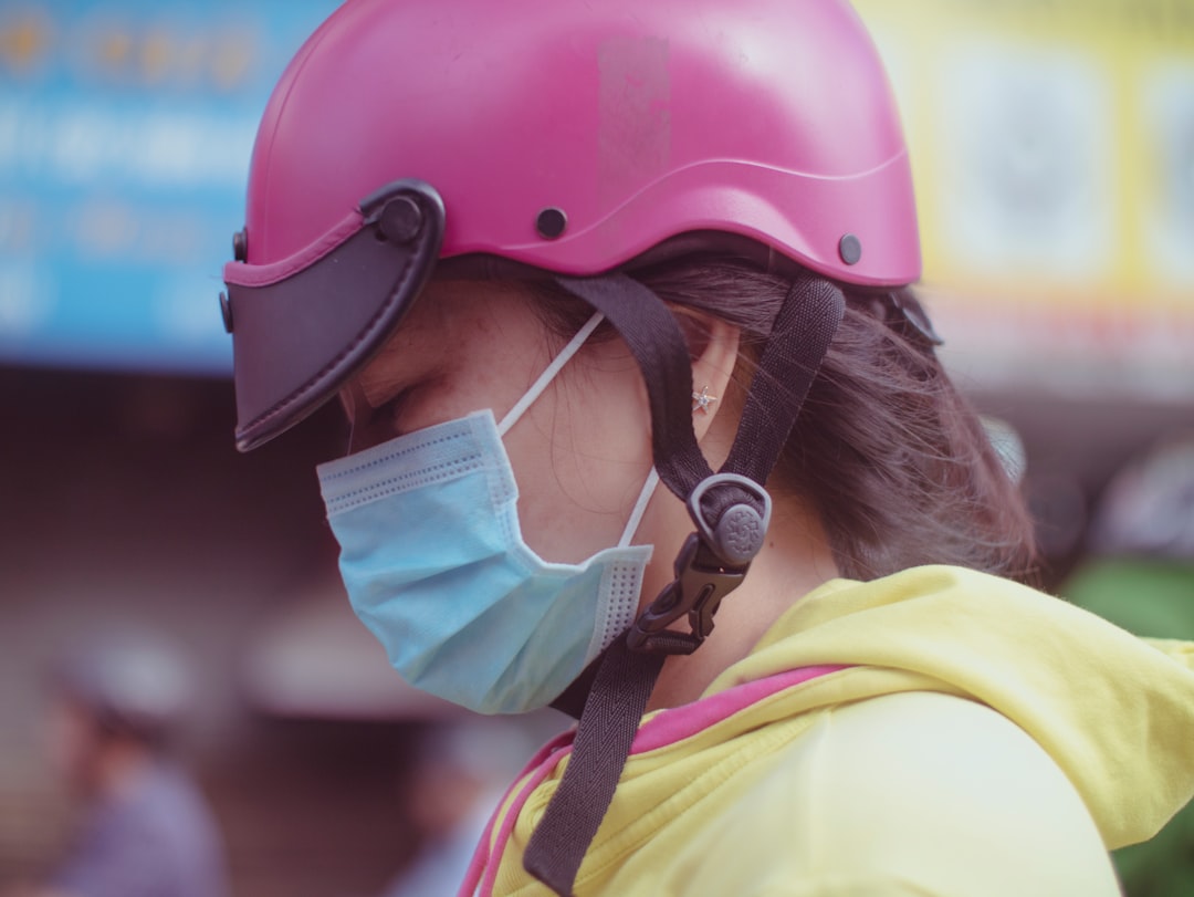 woman wearing yellow hooded jacket, green face mask, and pink helmet