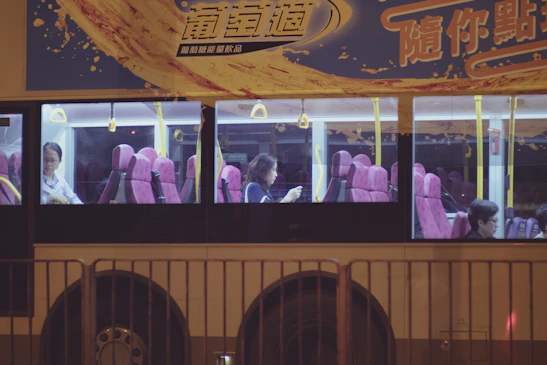 Passengers boarding a comfortable Tawang Alun Trans bus with pink accents under a clear blue sky.