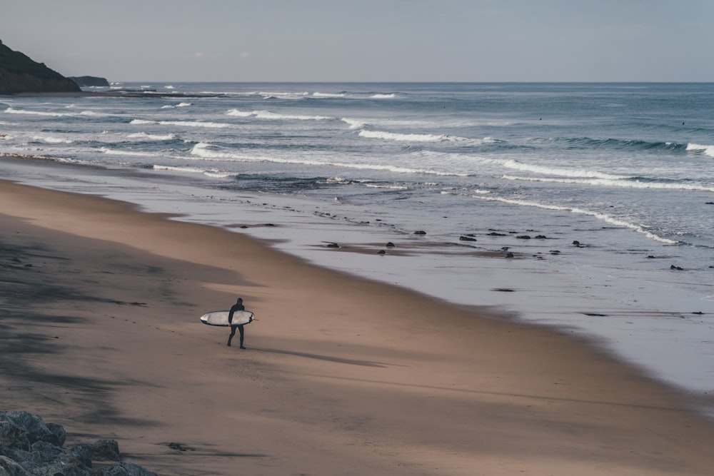 man holding surfboard walking on shore