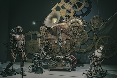 A steampunk-themed sculpture consisting of intricate gears and clockwork elements. The scene includes humanoid figures made from metal parts and adorned with mechanical features. A large horn-like element and clock dials are prominent, surrounded by various-sized cogs and gears.