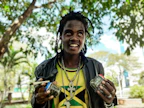 A smiling person holding a handful of colorful organic capsules outdoors.