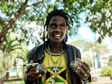 A smiling customer holding a small jar of rapé, surrounded by Amazonian plants.