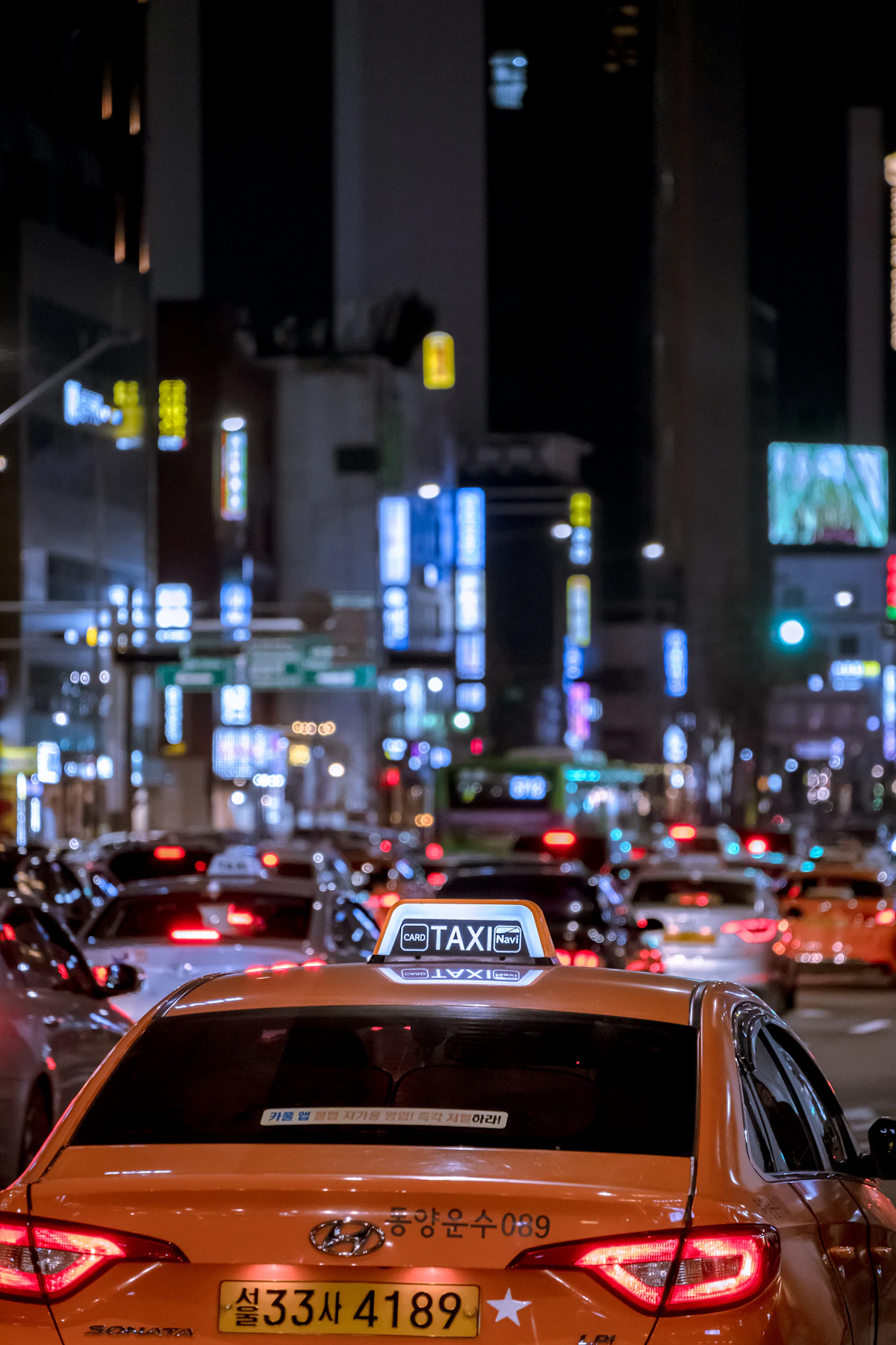 Orange Seoul taxi with a lit TAXI roof sign in night traffic