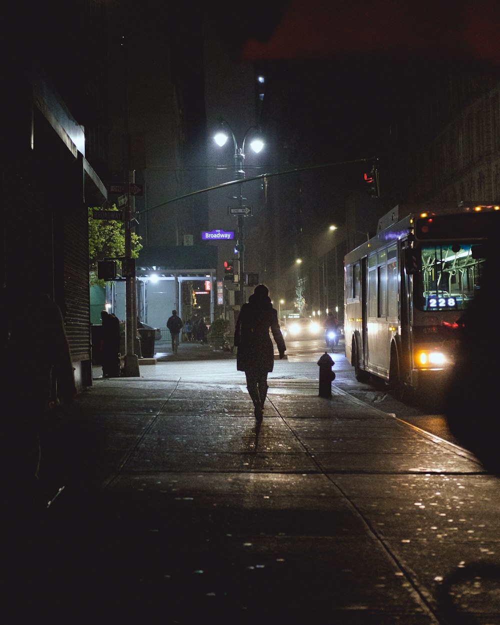 person walking on pathway near bus and vehicles during night time