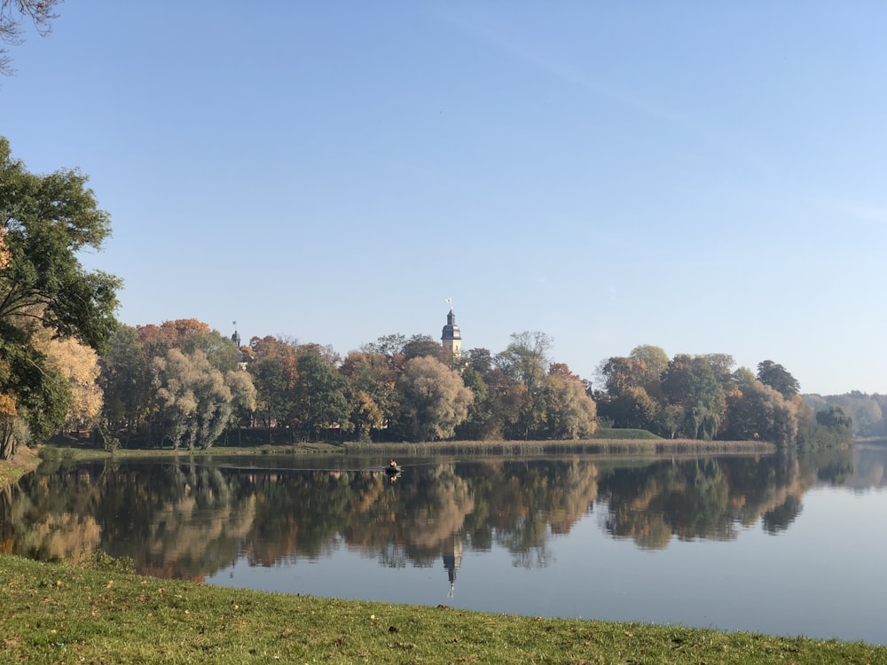 Vista lago circondato da alberi ad alto fusto e verdi sotto cieli azzurri e bianchi