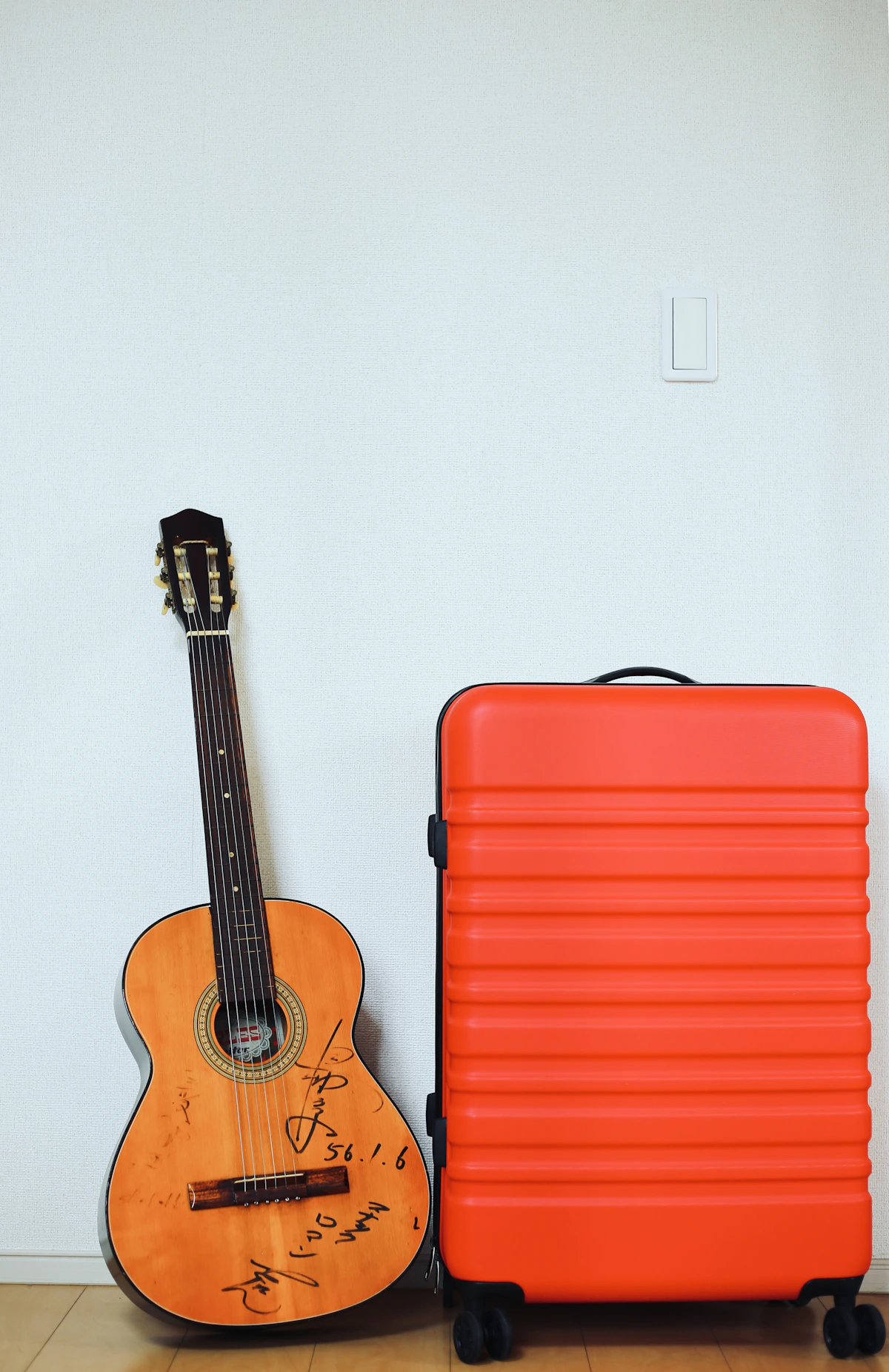 A red hard-shell suitcase is placed next to the guitar.