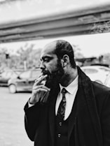 grayscale photo of man smoking standing near vehicles