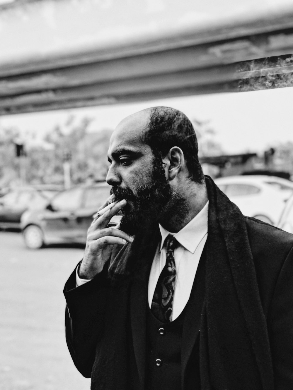 grayscale photo of man smoking standing near vehicles