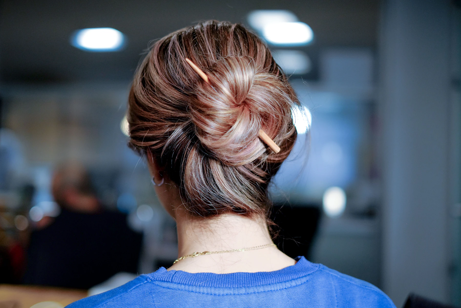 A twisted bun held in place by a wooden hair stick, seen from behind
