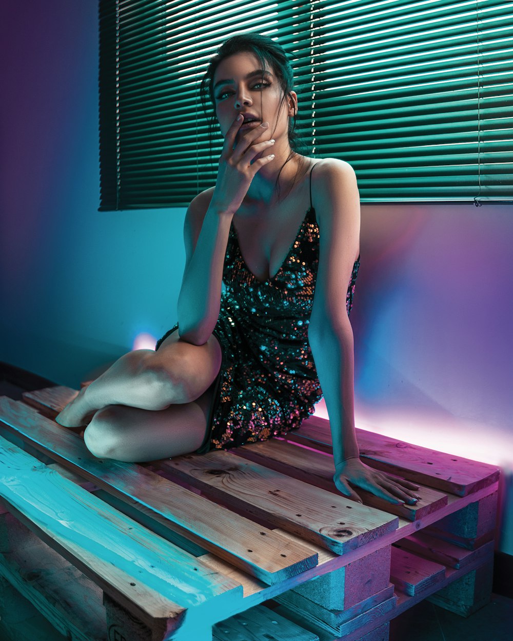 woman in black and gold floral dress sitting on wooden palettes by the window