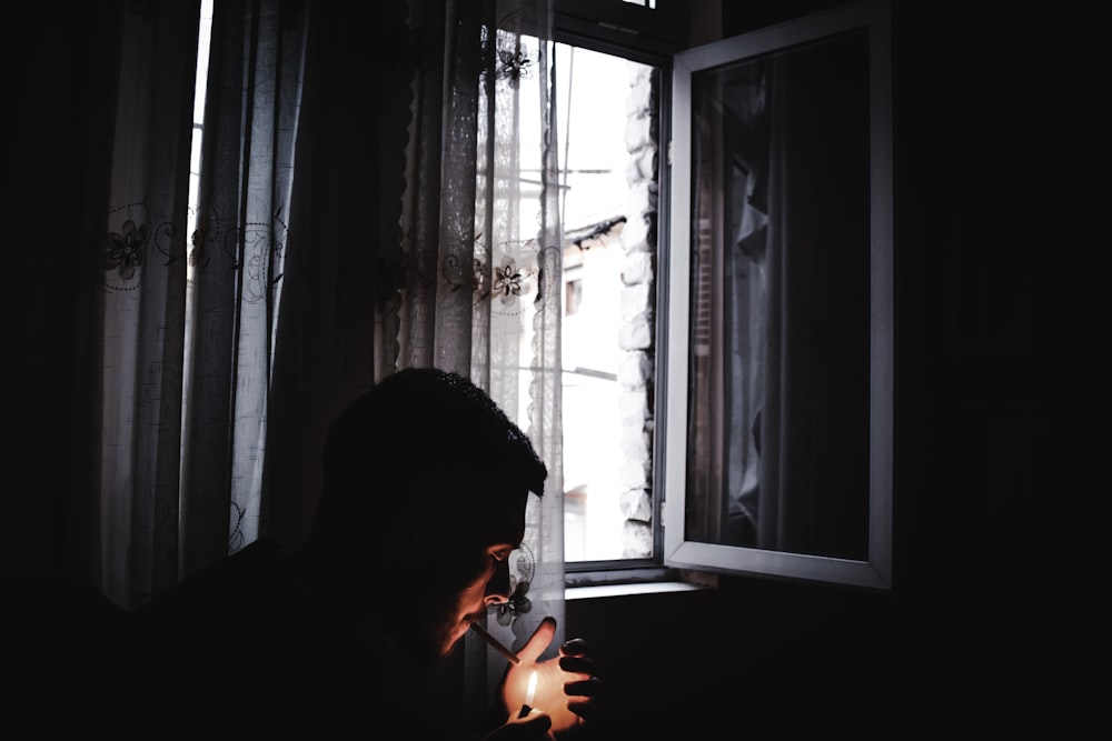 man lighting cigarette near window