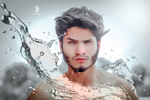 A surreal portrait of a young man with dark hair and facial hair, surrounded by artistic splashes of water, creating a dynamic and fluid effect. The water appears to be in motion, enhancing the vibrant and energetic composition. The background is blurred, focusing attention on the subject and the water.