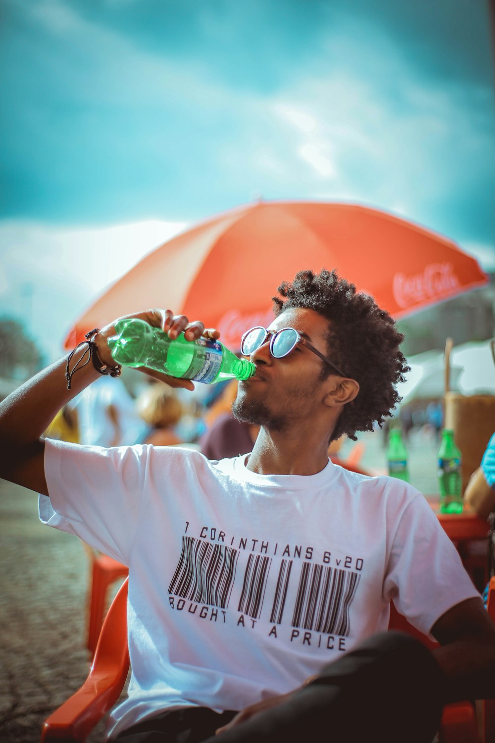 hombre sentado y bebiendo refresco cerca de la gente bajo cielos azules y blancos