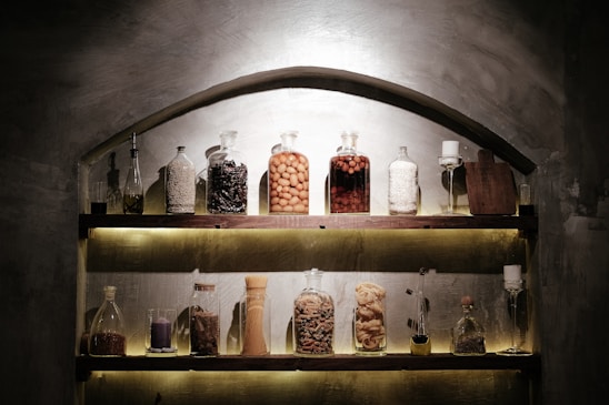 A rustic kitchen scene with jars of spices, bottles of olive oil, and homemade sauces arranged on a wooden table.