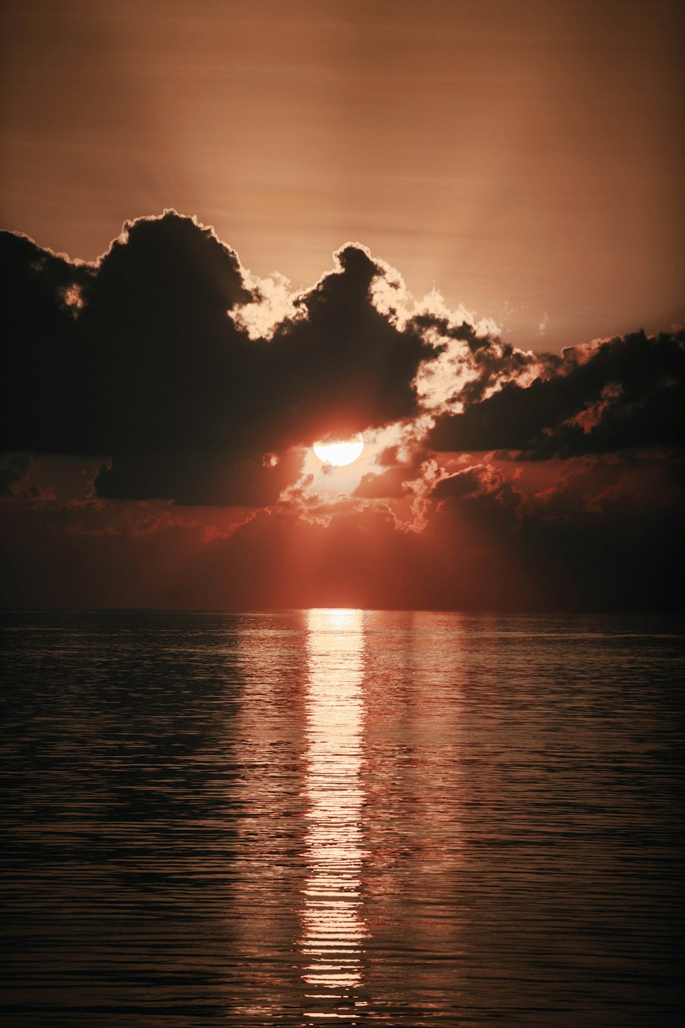 orange setting sun behind black clouds over the sea