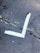 A white tape arranged in an L-shape on a cracked concrete surface. The concrete has several visible cracks and a rough texture, with a mix of grey shades and small spots of dirt.