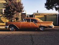 A vintage car parked on a cobblestone street under soft morning light.
