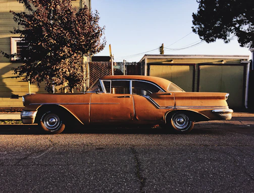 A classic vintage car parked beside a stone wall, bathed in warm afternoon light.