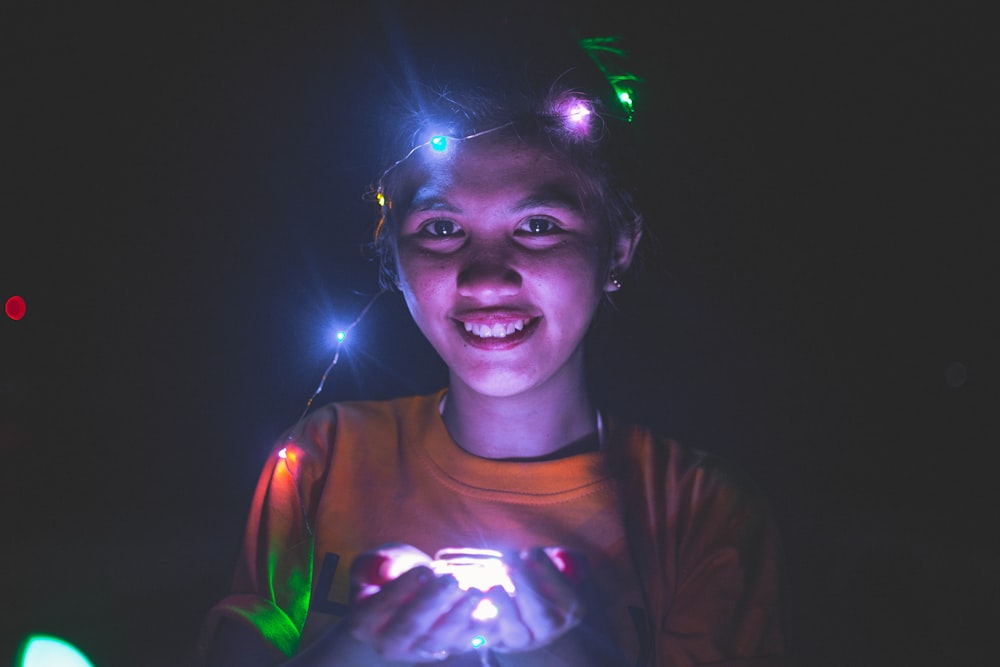 girl wearing and holding lighted string lights and smiling