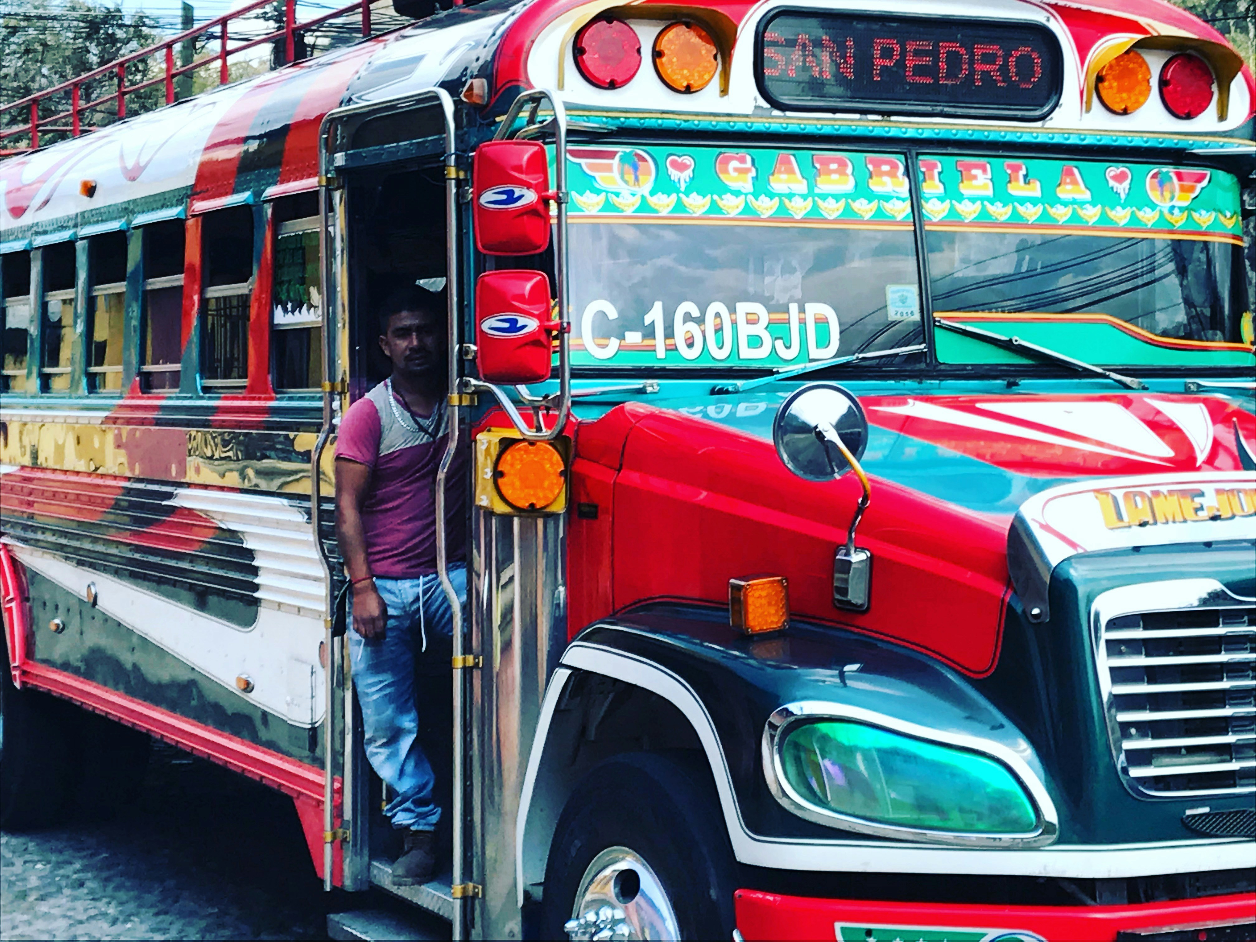 man on vehicle door, The public transportation system in Antigua, Guatemala, consists of these repurposed and colorfully painted school buses.