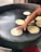 A person is cooking flatbreads on a large circular griddle, with a hand pressing down on one of the flatbreads. There are several other flatbreads in various stages of cooking on the griddle.