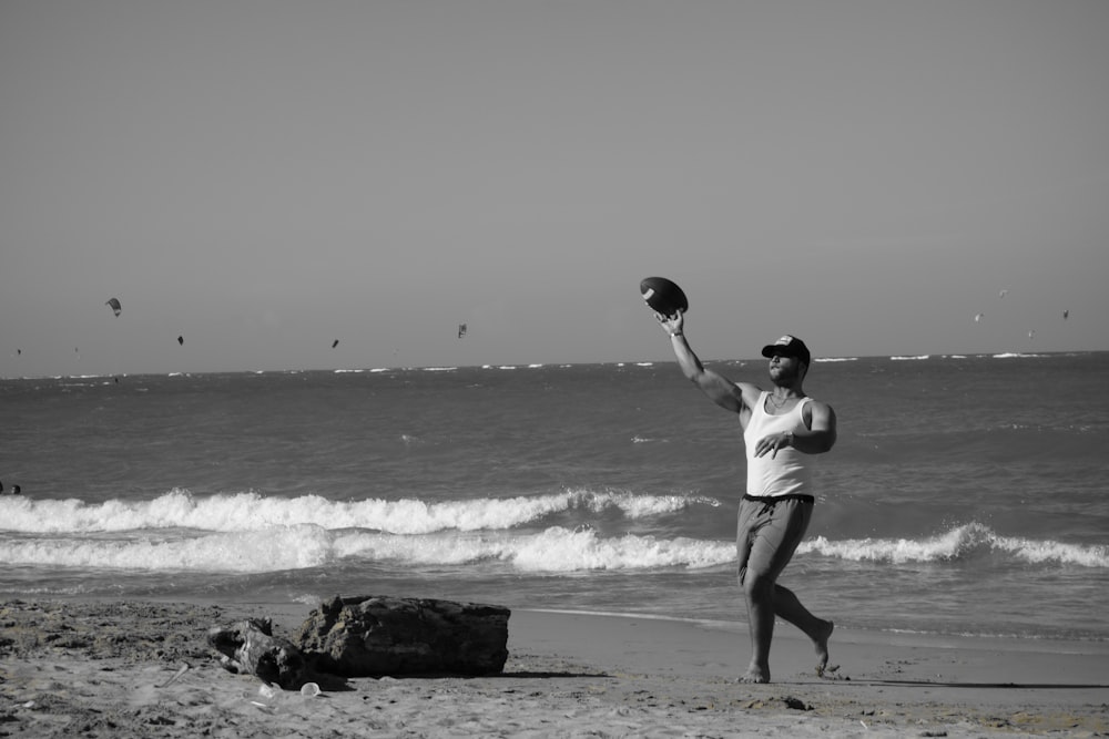 grayscale photo of man catching disc plate on seashore