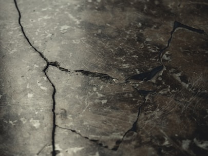 A close-up view of a cracked and weathered concrete surface with visible fractures and dark lines running through it.