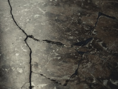 A close-up view of a cracked and weathered concrete surface with visible fractures and dark lines running through it.