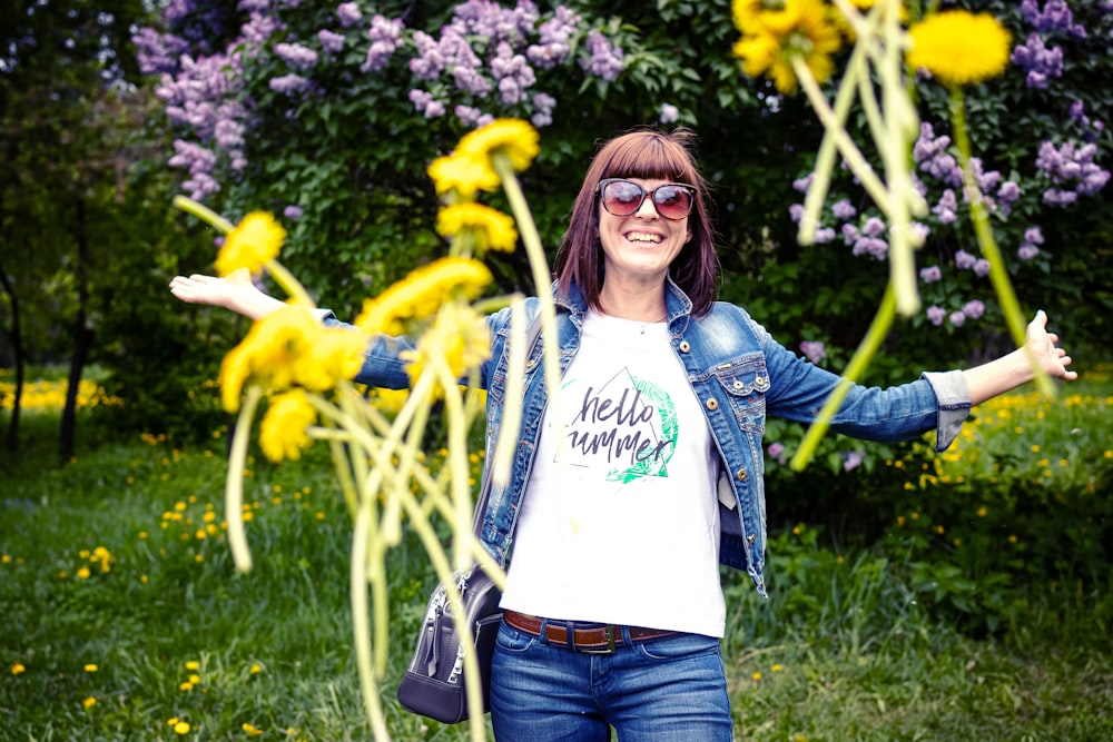 smiling woman standing and raising both hands in green field surrounded with tall and green trees