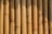 A close-up view of vertically aligned, natural bamboo stalks. The bamboo displays varying shades of light brown and tan, featuring some natural blemishes and knots. Sunlight creates shadows and highlights on the surface, emphasizing the texture and natural grains.