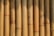 A close-up view of vertically aligned, natural bamboo stalks. The bamboo displays varying shades of light brown and tan, featuring some natural blemishes and knots. Sunlight creates shadows and highlights on the surface, emphasizing the texture and natural grains.
