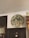 A circular emblem is mounted on an interior wall above a doorway. The emblem reads 'Shire of Sherbrooke 1889' and features palm tree graphics and a central design resembling an anchor or symbol. Nearby, there's a decorative mirror with an ornate frame, and a clothing rack is partially visible.