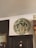 A circular emblem is mounted on an interior wall above a doorway. The emblem reads 'Shire of Sherbrooke 1889' and features palm tree graphics and a central design resembling an anchor or symbol. Nearby, there's a decorative mirror with an ornate frame, and a clothing rack is partially visible.
