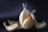 A close-up of a garlic bulb with several cloves partially peeled, set against a dark background with soft lighting highlighting the texture of the skin.