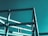 A partially constructed steel framework structure against a solid teal-colored sky. The metal beams intersect at various angles, forming geometric patterns and suggesting an industrial or architectural setting.