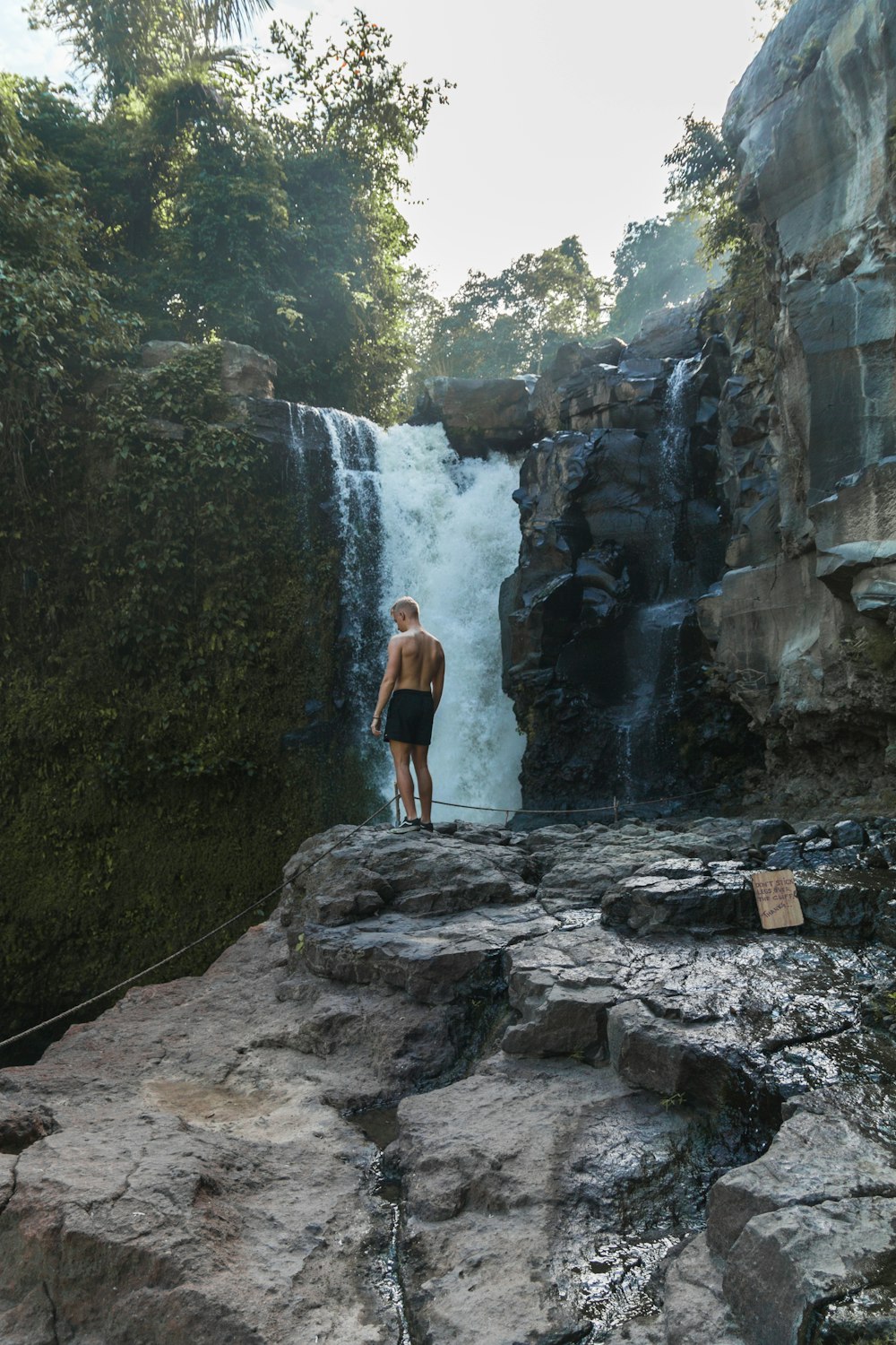 man standing on cliff near waterfall