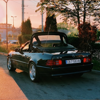 A classic convertible with its top down, parked near the dealership entrance on a warm afternoon.