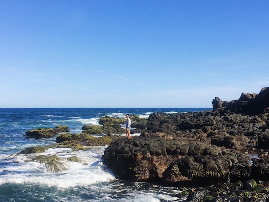 woman standing alone on beach cliff viewing sea under blue and white skies in Pulpit Rock Australia